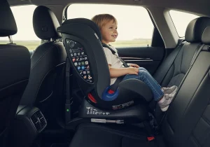 Copil așezat într-un scaun auto montat cu spatele la sensul de mers, oferind protecție maximă.

